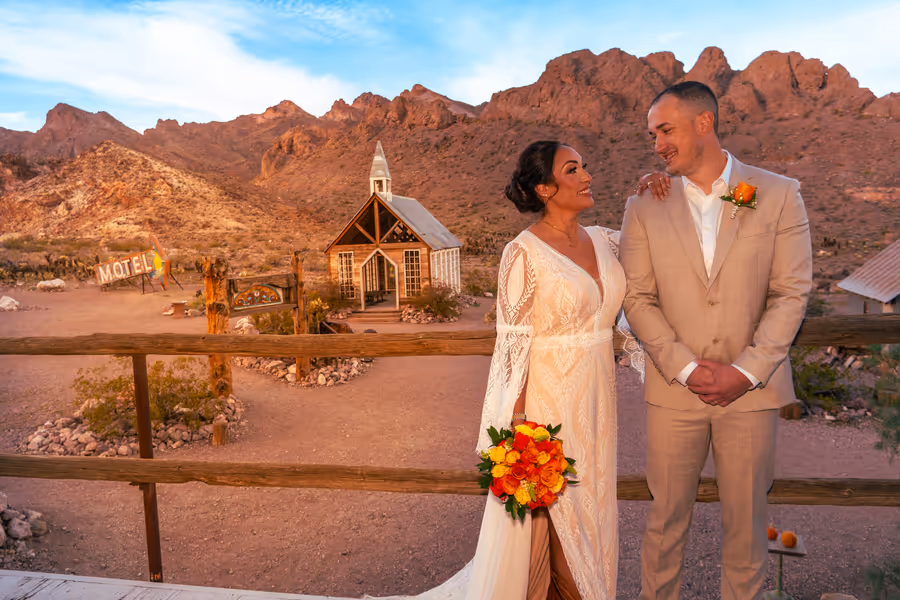 Bride and groom at golden hour above the little white chapel and desert mountains at Nelson Ghost Town, Nevada