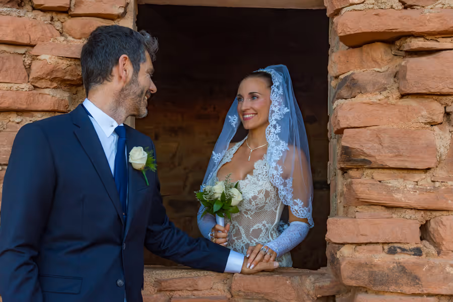 Bride in a lace veil smiling at the groom through a window of the historic sandstone cabins at Valley of Fire State Park