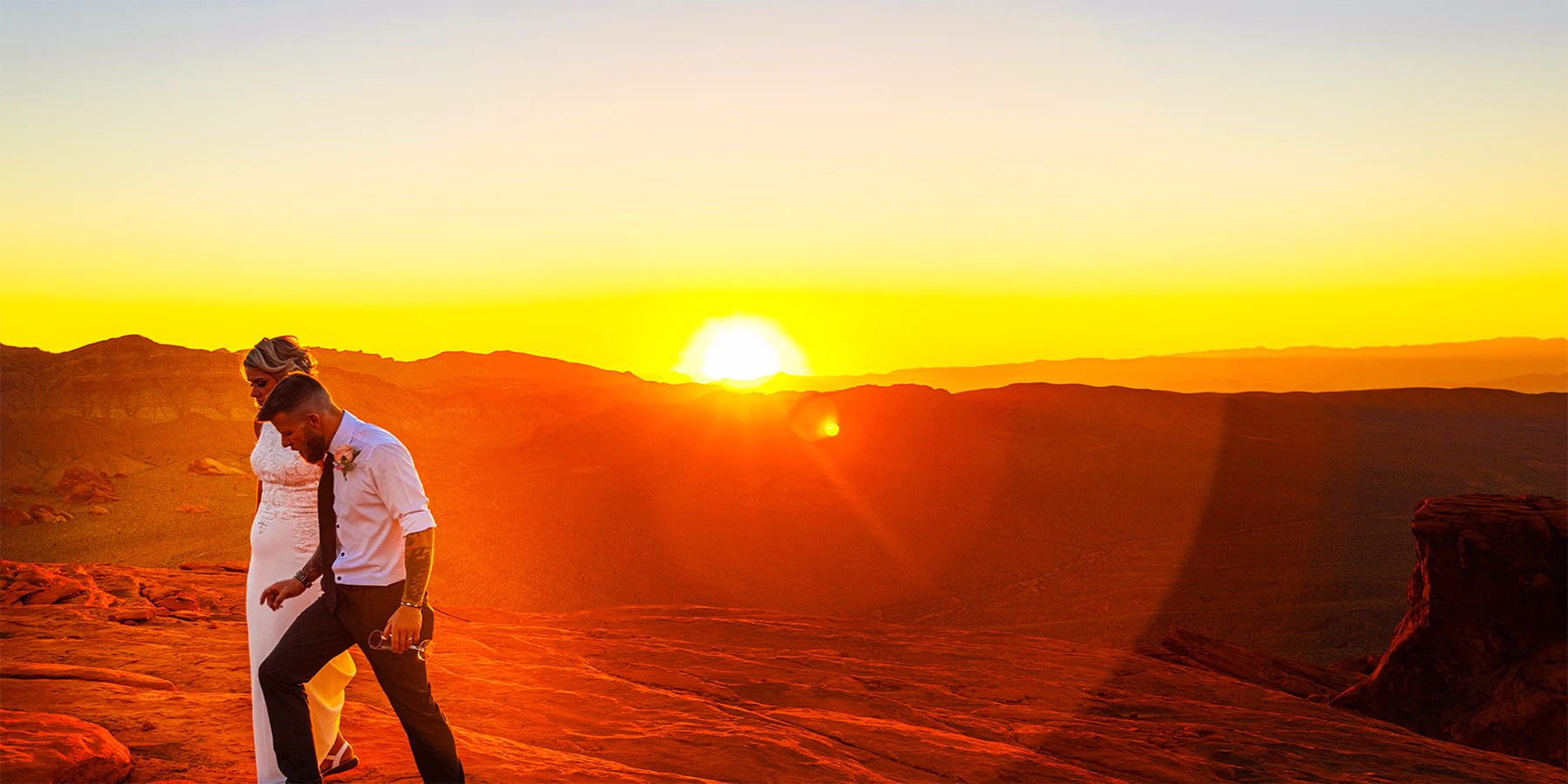 Helicopter wedding couple on red rock plateau at Valley of Fire Nevada at golden sunset — private peak landing Las Vegas