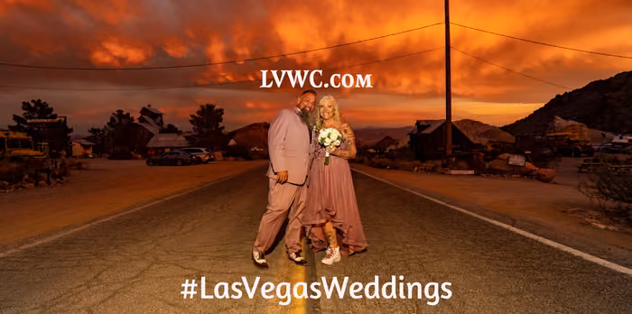 Married couple standing on the road under a dramatic orange sunset sky at Nelson Ghost Town Nevada